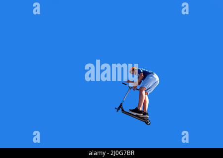 boy jumping with his Push scooter under blue sky Stock Photo