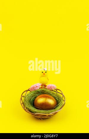Easter composition with a yellow chicken and a gilded egg in a nest on a yellow background with a copy space Stock Photo