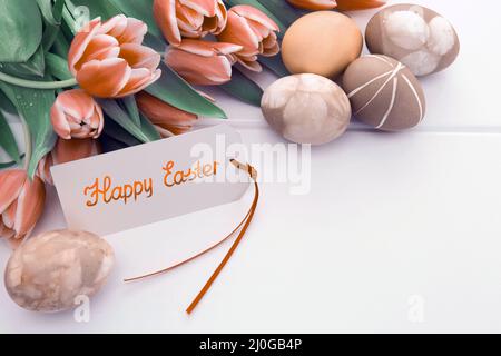 Easter card with bouquet of tulips and colorful eggs on white wooden . Stock Photo