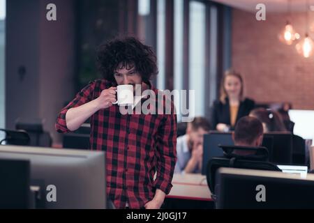 Smiling businessman in afro shirt standing in modern office with cup of coffee in hand. Selective focus  Stock Photo