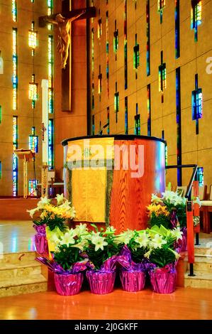 Pulpit with flowers seen in the Annunciation of the Blessed Virgin Mary Catholic Church. The background shows a crucified Jesus Christ and stained gla Stock Photo