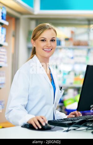 Let me bring up your details on the computer. Shot of a young pharmacist using a computer at the checkout counter. Stock Photo