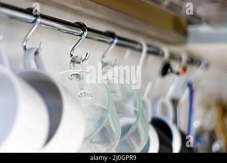 A set of mugs hanging on hooks in a modern home kitchen Stock Photo