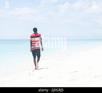 Black African young man walking on tropical beach Stock Photo