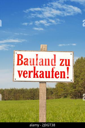 Sign on a green field with the German text: Bauland zu verkaufen (Building land for sale!) in po Stock Photo