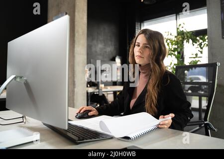 Design and architecture theme. A female young architect is working on a project with blueprints at the computer in a modern offi Stock Photo