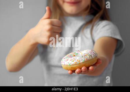 The child shows with a gesture - thumbs up - that the donut is very tasty and you need to buy it Stock Photo