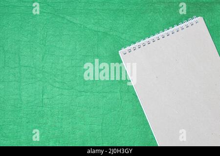 White and gray notepad sheet with spiral against the background of green fabric. Concept of analysis, study, attentive work. Stock photo with empty place for your text and design. Stock Photo