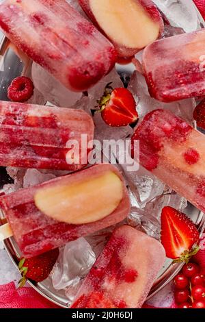 Strawberry raspberry apple and red currant ice cream popsicles in metal tray with ice cubes Stock Photo