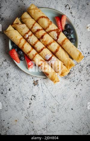 Plate of delicious crepes roll with fresh fruits and chocolate Stock Photo