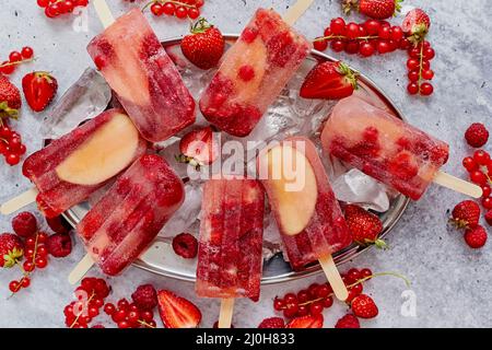 Homemade raspberry, strawberry, apple and currant popsicles on metal plate with ice assorted berries Stock Photo
