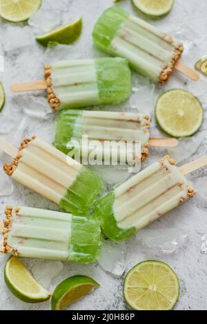 Lime and cream homemade popsicles or ice creams placed with ice cubes on gray stone backdrop Stock Photo