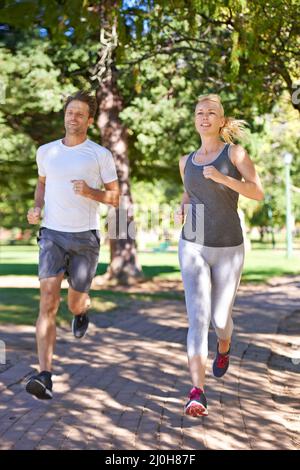 Burning calories as a couple. A couple in sportswear jogging through the park. Stock Photo