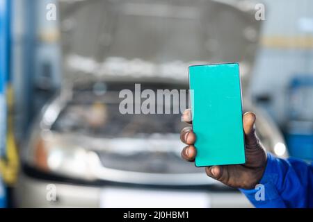 close shot of car machanic hands using green screen mobile phone with uniform in front of car - concept of online booking service, advertisement and Stock Photo