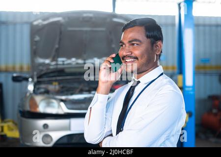 Supervisor or manager busy talking on mobile phone at garage about car repair or maintenance service - concept of customer service, communication and Stock Photo
