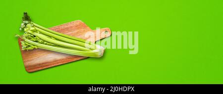 Celery branch bunch on a cutting board. Isolated on green banner background Stock Photo