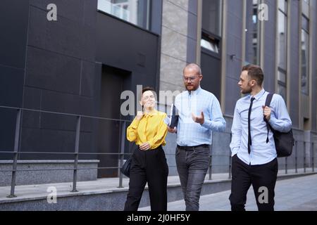 Business people outdoors. Three white collar workers in formal wear walking along the street during the break at office, urban background. Brainstorming or discussing project. High quality photo Stock Photo