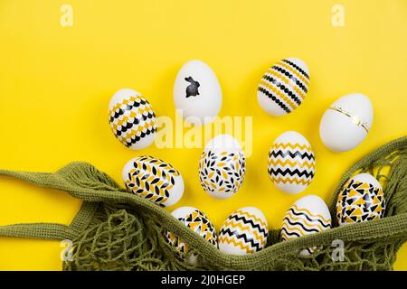 Golden, black, white eggs in a string bag on a yellow background. View from above. Easter card with copy space for text Stock Photo