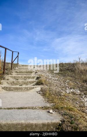 Ladder going up. Staircase made of concrete steps against the blue sky. Railings from metal pipes. Climbing up. Close-up. Selective focus. Copy space. Stock Photo