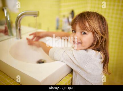 I can reach the tap now. A cute little girl washing her hands in the bathroom basin. Stock Photo