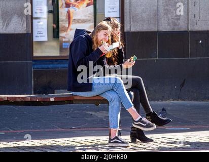 Dundee, Tayside, Scotland, UK. 19th Mar, 2022. UK Weather: As a result of the warm March sunshine, temperatures in parts of North East Scotland reached 15°C. Locals are out and about in Dundee's city centre, taking advantage of the nice weather and socialising. In the afternoon sunshine, two fashionable young women seated on a summer seat enjoy a bite to eat. Credit: Dundee Photographics/Alamy Live News Stock Photo