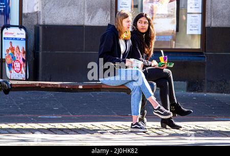 Dundee, Tayside, Scotland, UK. 19th Mar, 2022. UK Weather: As a result of the warm March sunshine, temperatures in parts of North East Scotland reached 15°C. Locals are out and about in Dundee's city centre, taking advantage of the nice weather and socialising. In the afternoon sunshine, two fashionable young women seated on a summer seat enjoy a bite to eat. Credit: Dundee Photographics/Alamy Live News Stock Photo