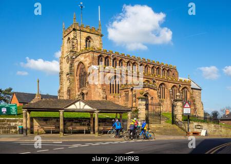 Cyclists stopped for a rest outside the parish church of  St James the Great in the Cheshire village of Audlem, Stock Photo