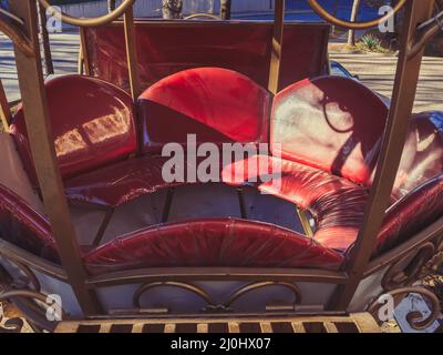 Red decorative leather seat in a metal street carriage on a sunny day Stock Photo