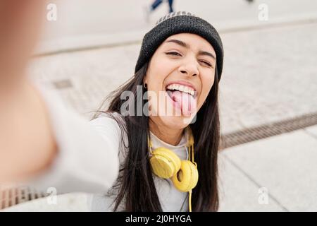 latina taking a selfie with her smart phone sticking out her tongue and winking. Hispanic woman making a funny face while taking a selfie Stock Photo