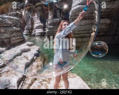 The girl blows huge soap bubbles into the canyon gorge near the clear river. View through the bubble Stock Photo
