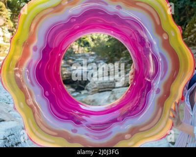 Bright inflatable swimming ring with multicolored striped pattern in nature. View through the hole. Closeup photo Stock Photo