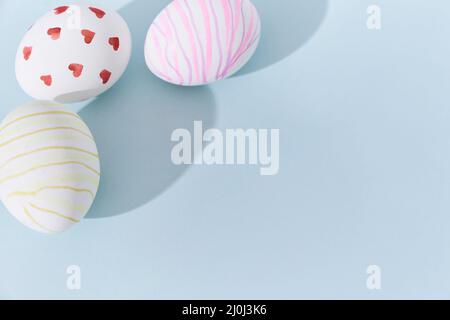 Close-up of three Easter eggs with a pattern of hearts and lines on a blue background. A shadow in the background. With space to copy. High quality photo Stock Photo