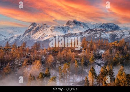 Amazing red and orange sunset over snow capped mountains on a Winter evening in the English Lake District. Dramatic scenic landscape of Great Britain. Stock Photo