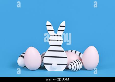 Striped black and white and pink easter bunny ornament and eggs on blue background Stock Photo