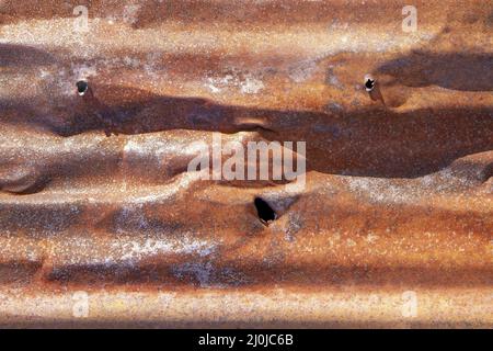 Brown abstract background with silver red hues. A weathered, rust-eaten, crumpled, perforated textured sheet of metal. Stock Photo