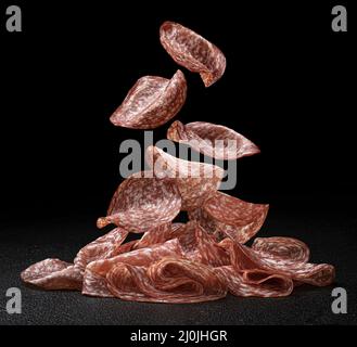 Falling salami slices isolated on black background Stock Photo