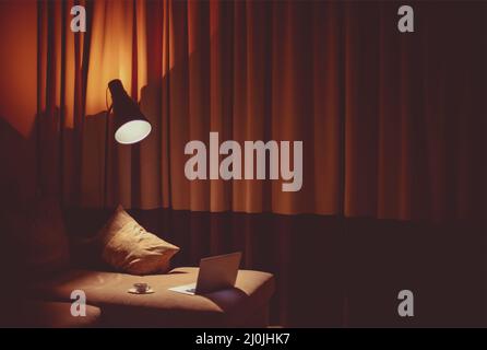 Opened laptop on a gray sofa with cup of coffee in the night cozy room Stock Photo