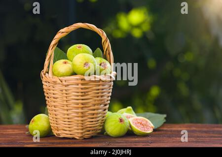 Fresh figs in basket on wooden table. Background with fig garden in autumn Stock Photo