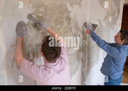 Young caucasian couple removing old wallpaper from walls preparing for flat renovation. Stock Photo