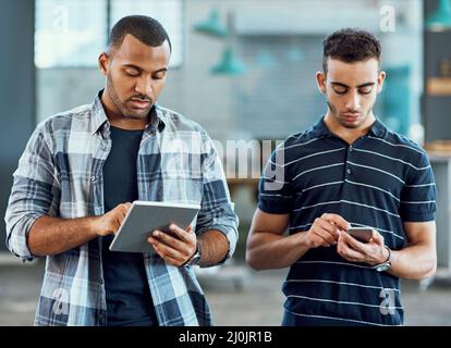 Caught up in a connected world. Shot of two young designers using digital devices in an office. Stock Photo