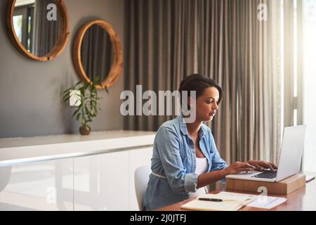 Managing pregnancy and her monthly bills. Shot of a pregnant young woman using a laptop while working from home. Stock Photo