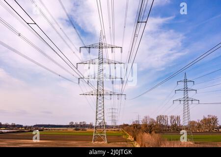 Many high-voltage pylons in a row in rural area for German Energiewende seen from drone perspective, Germany Stock Photo