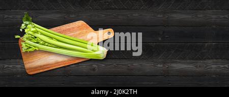 Celery branch bunch on a cutting board. Isolated on black wood banner background Stock Photo