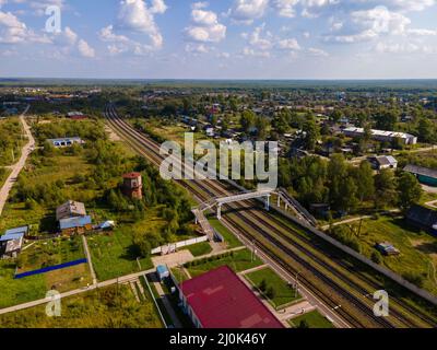 Railroad between trees and houses under cloudy blue sky Stock Photo