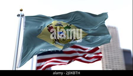 The flag of the US state of Delaware waving in the wind with the American stars and stripes flag blurred in the background Stock Photo