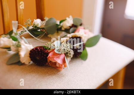 Brides wreath of white and pink roses, branches of eucalypt tree and burgundy chrysanthemum with thin ribbons on a textile beige Stock Photo