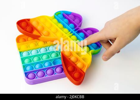 Anti-stress game Pop it. A child's hand presses the finger of colored bubbles on a toy in the shape of a butterfly. Stock Photo