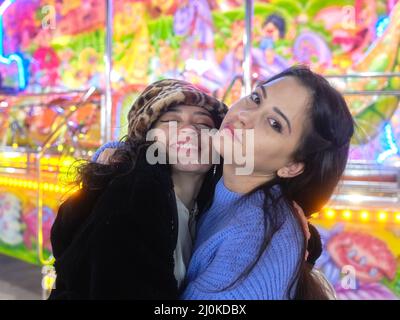 Portrait of two woman embracing while facing the camera in a night fair Stock Photo