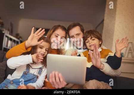 Chatting with family all across the globe. Cropped shot of an affectionate young family of four video chatting using a digital tablet on the sofa at Stock Photo