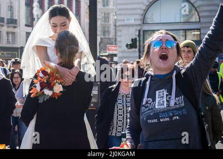 Protest taking place against vaccinating children for Covid 19, joined by anti-vaxxers, passing a bride and groom during a photoshoot Stock Photo